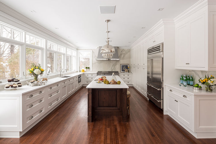 Bright white kitchen with a central island, large windows, stainless steel appliances, and warm wood flooring.