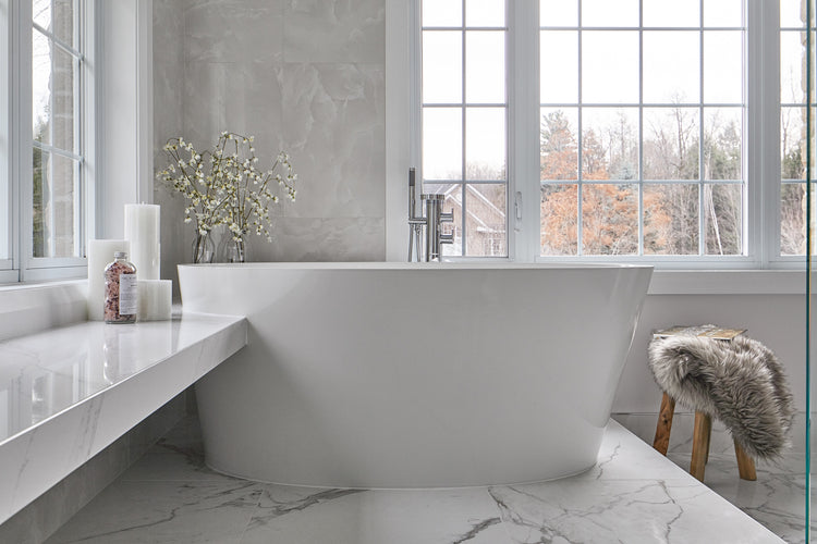 Minimalist bathroom with a freestanding tub by large windows, marble surfaces, and soft natural decor.