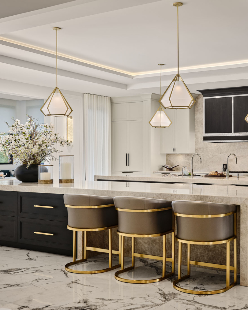 Elegant kitchen with a large island, gold-accented bar stools, pendant lighting, and marble surfaces.