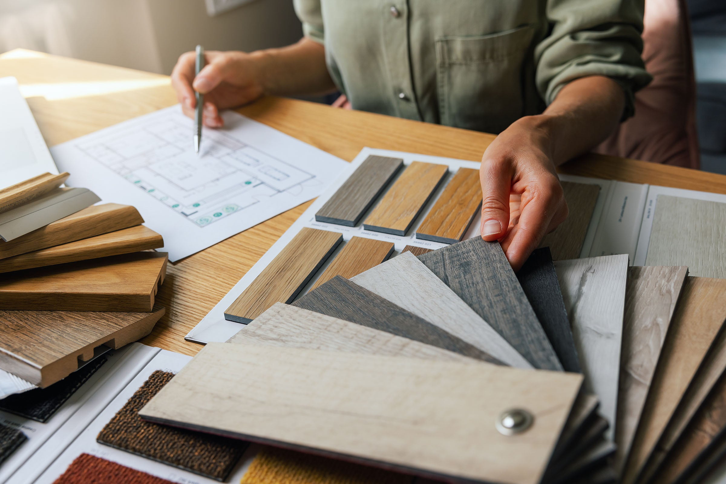 Designer reviewing material samples and floor plans at a desk with wood swatches and finish options.