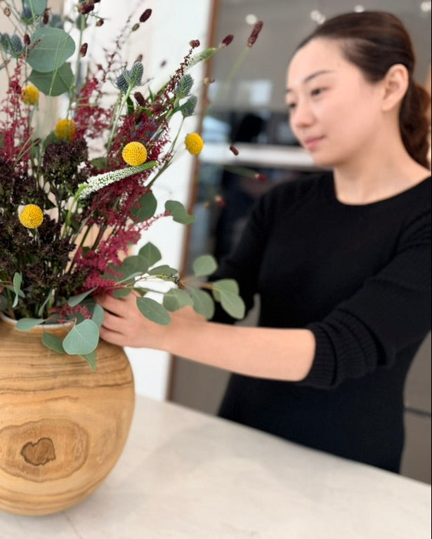Person arranging flowers in a wooden vase indoors