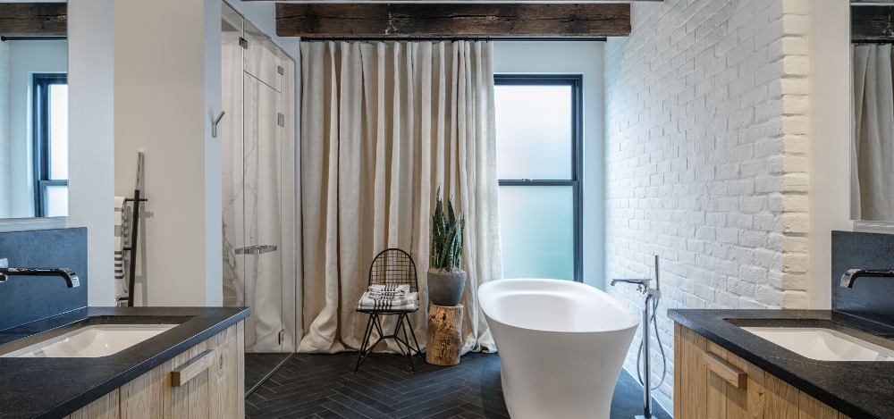 Modern bathroom with a freestanding tub, white brick wall, dual vanities, and a walk-in shower framed by soft curtains and natural wood accents