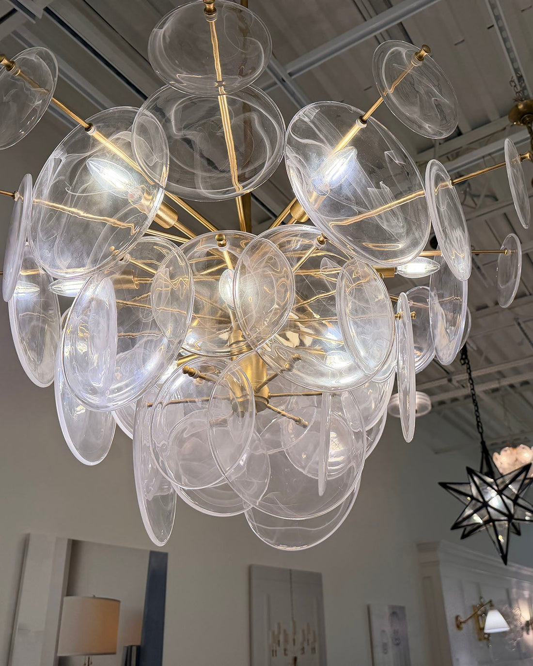 Chandelier with clear glass discs and gold fixtures in a room setting.
