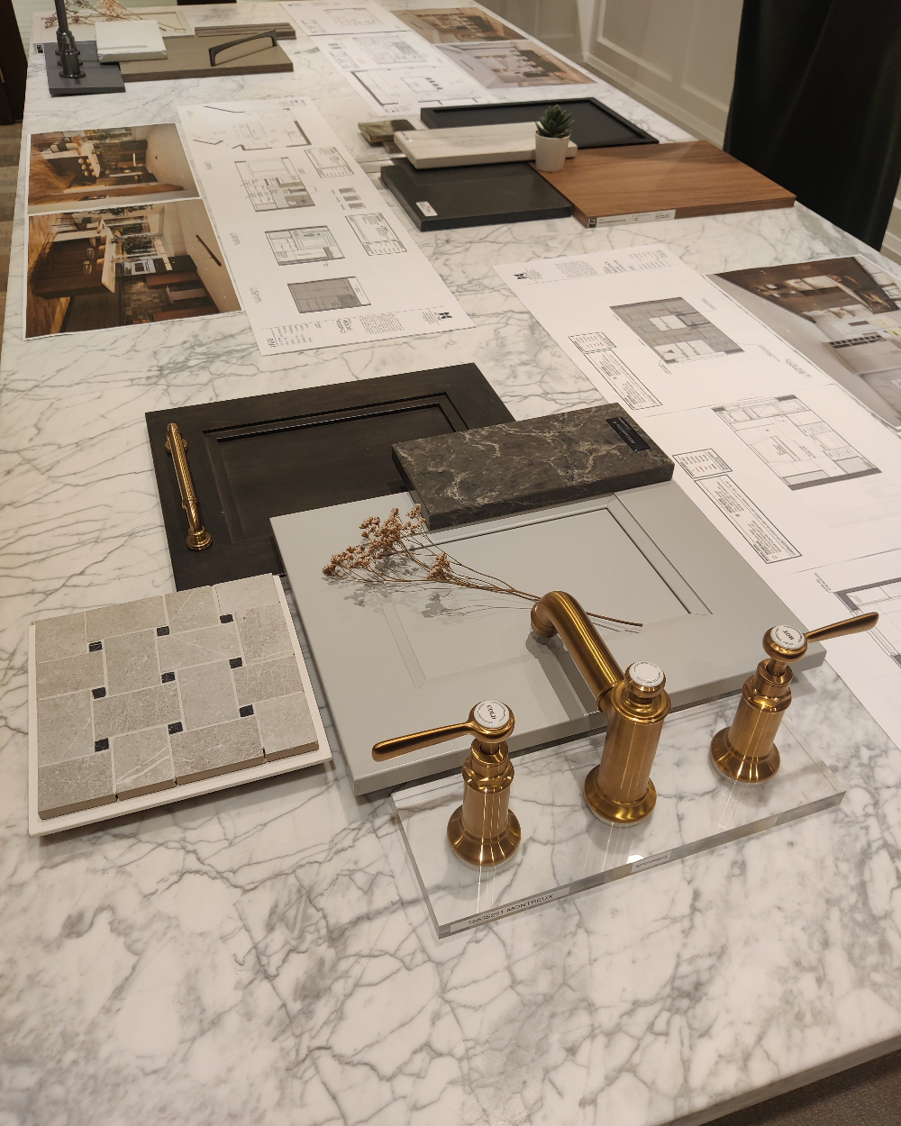 Gold faucet on a marble surface with design plans and samples in the background
