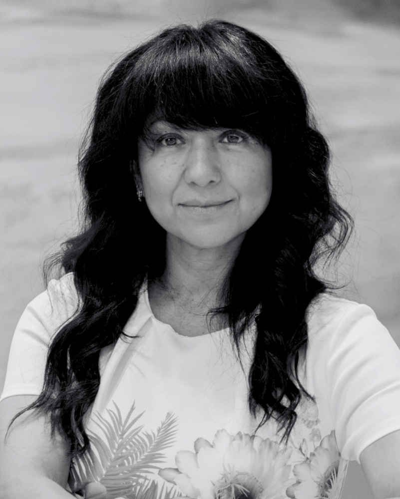 Black and white photo of a person with long dark hair wearing a light-colored top with a floral design.