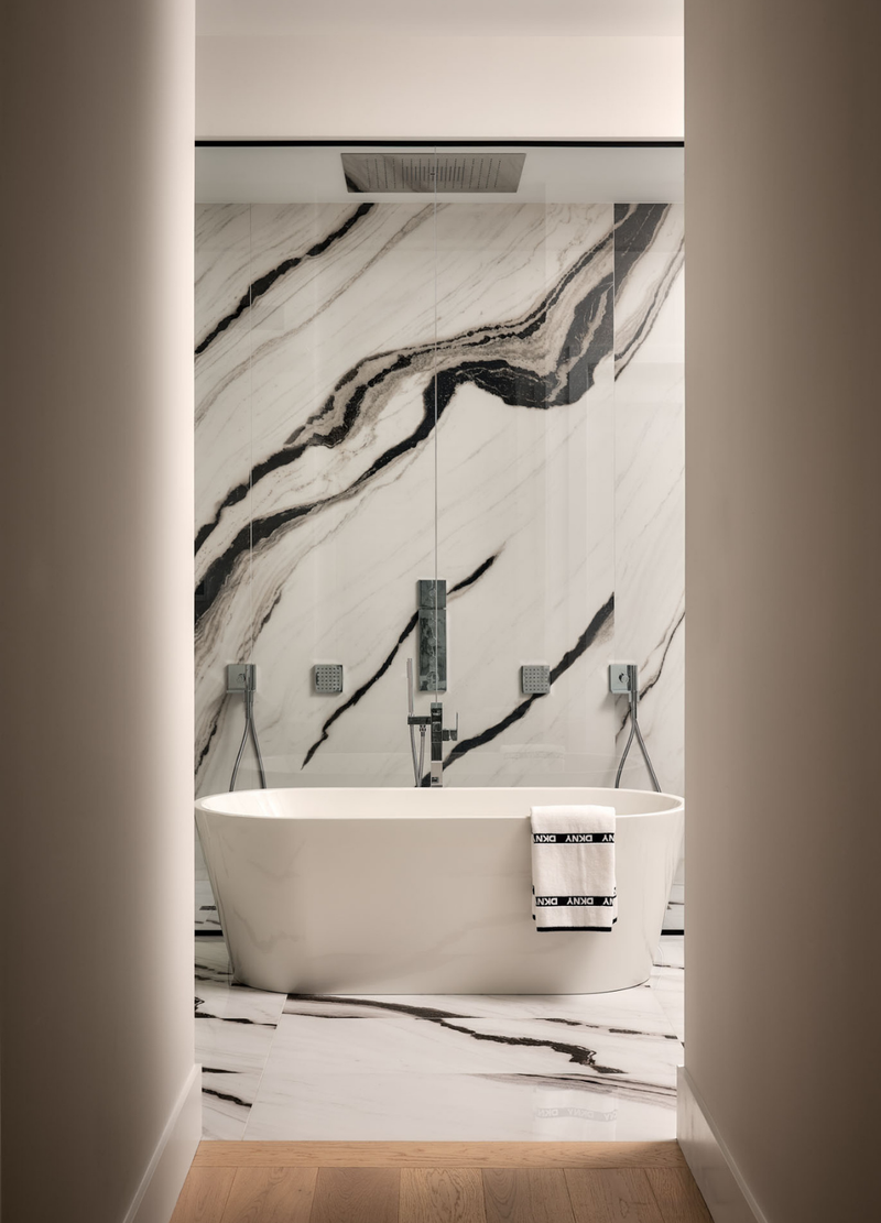 Modern bathroom with a freestanding bathtub against a marble-patterned wall.